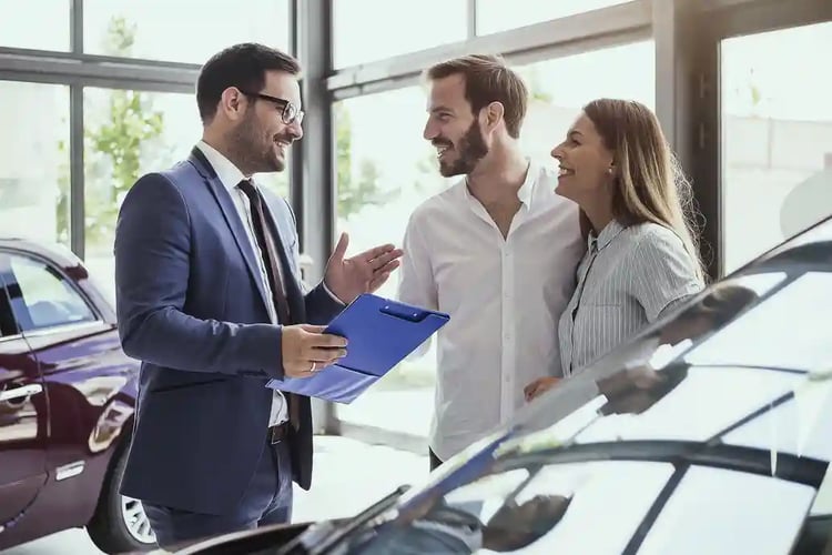 A young couple listening to the salesperson as they contemplate buying a new vehicle. 